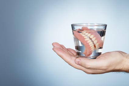 Man holding a glass containing old dentures, what are dentures